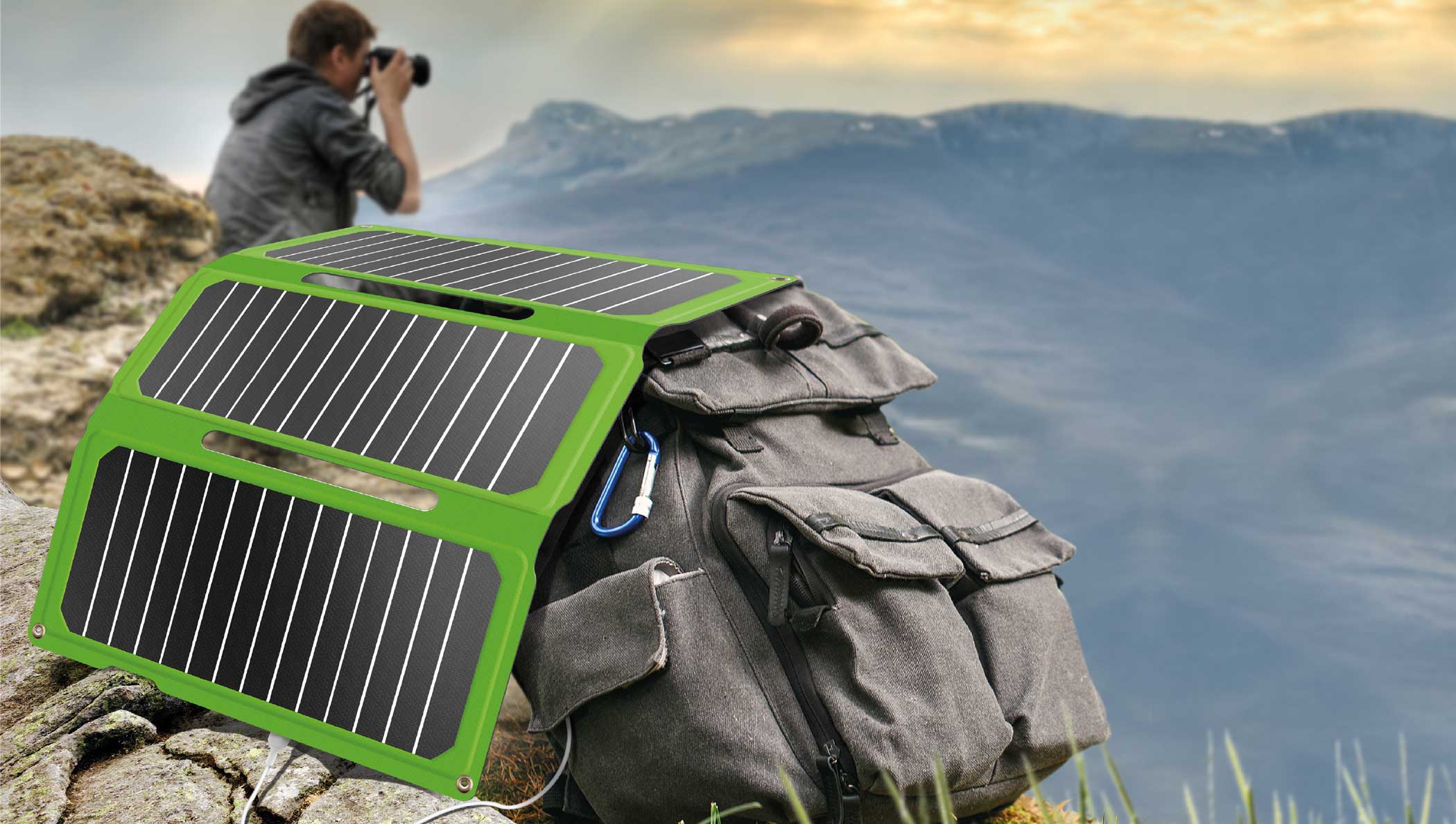 Panneau solaire portable vert replié posé sur un sac à dos gris en montagne, avec homme photographe au loin. Panneau solaire portable vert replié posé sur un sac à dos gris en montagne, avec homme photographe au loin.