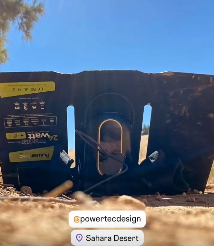 Panneau solaire portable Powertec posé au sol dans le Sahara, encadré par un fond désertique, avec étiquette jaune et poignée, vue à travers une ouverture.